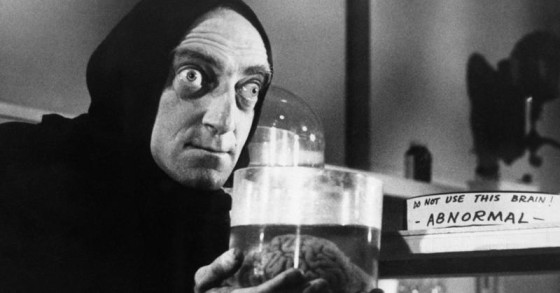 A still from the movie Young Frankenstein showing Igor (pronounced eye-gore) holding a brain in a jar next to a label that reads 'do not use this brain! -abnormal-'. He's wearing a black apocalypse cloak